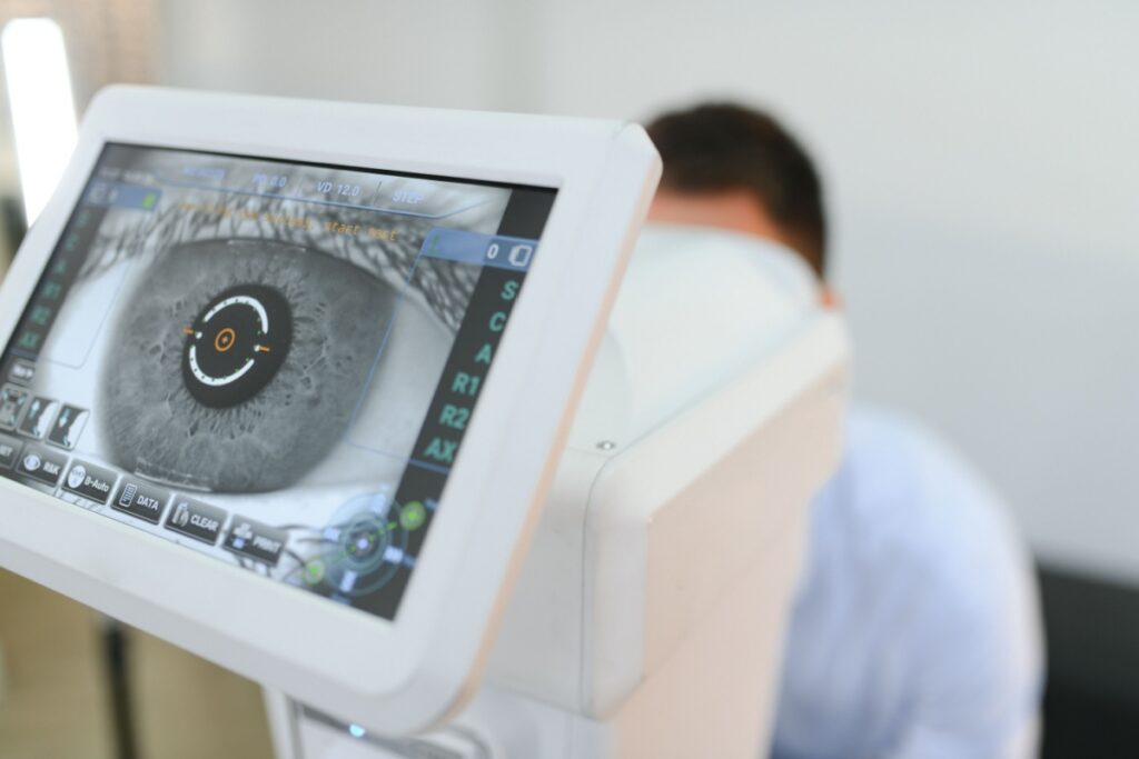 Digital diagnostic eye exam screen displaying a corneal scan while a patient is positioned behind the machine.