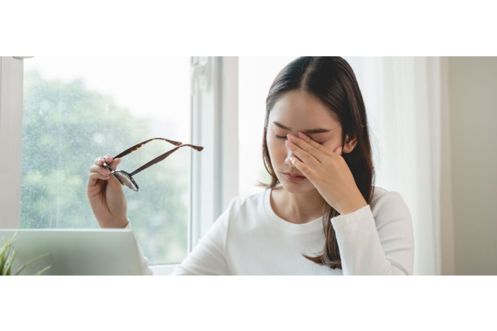 Young woman rubbing her eyes while holding her glasses.